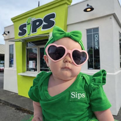 Sips' littlest fan in a green bow and heart sunglasses in front of the stand